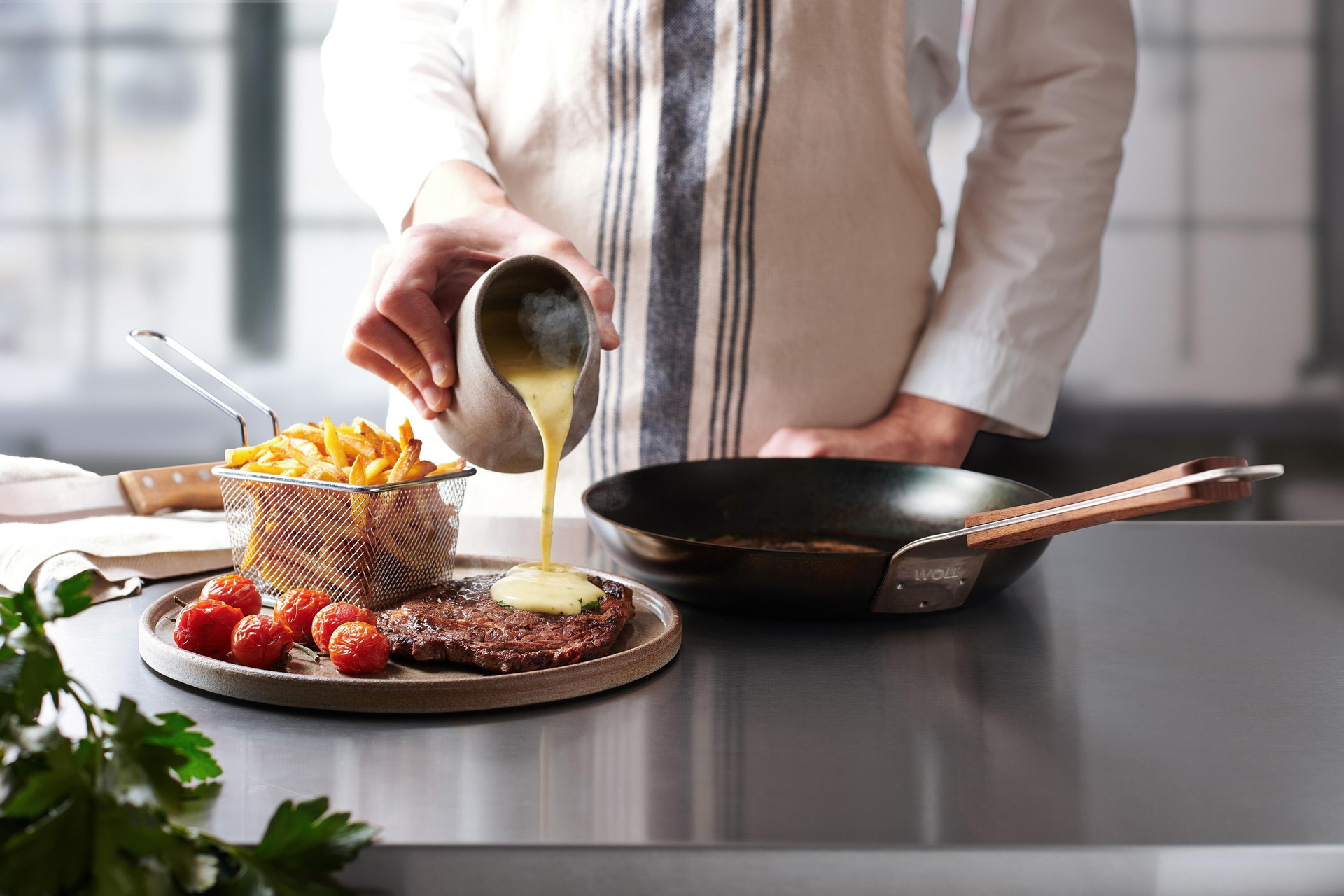 Auf einem Teller liegt ein angebratenes Steak, das mit Soße übergossen wird. Daneben steht eine runde Carbon Steel Pfanne.