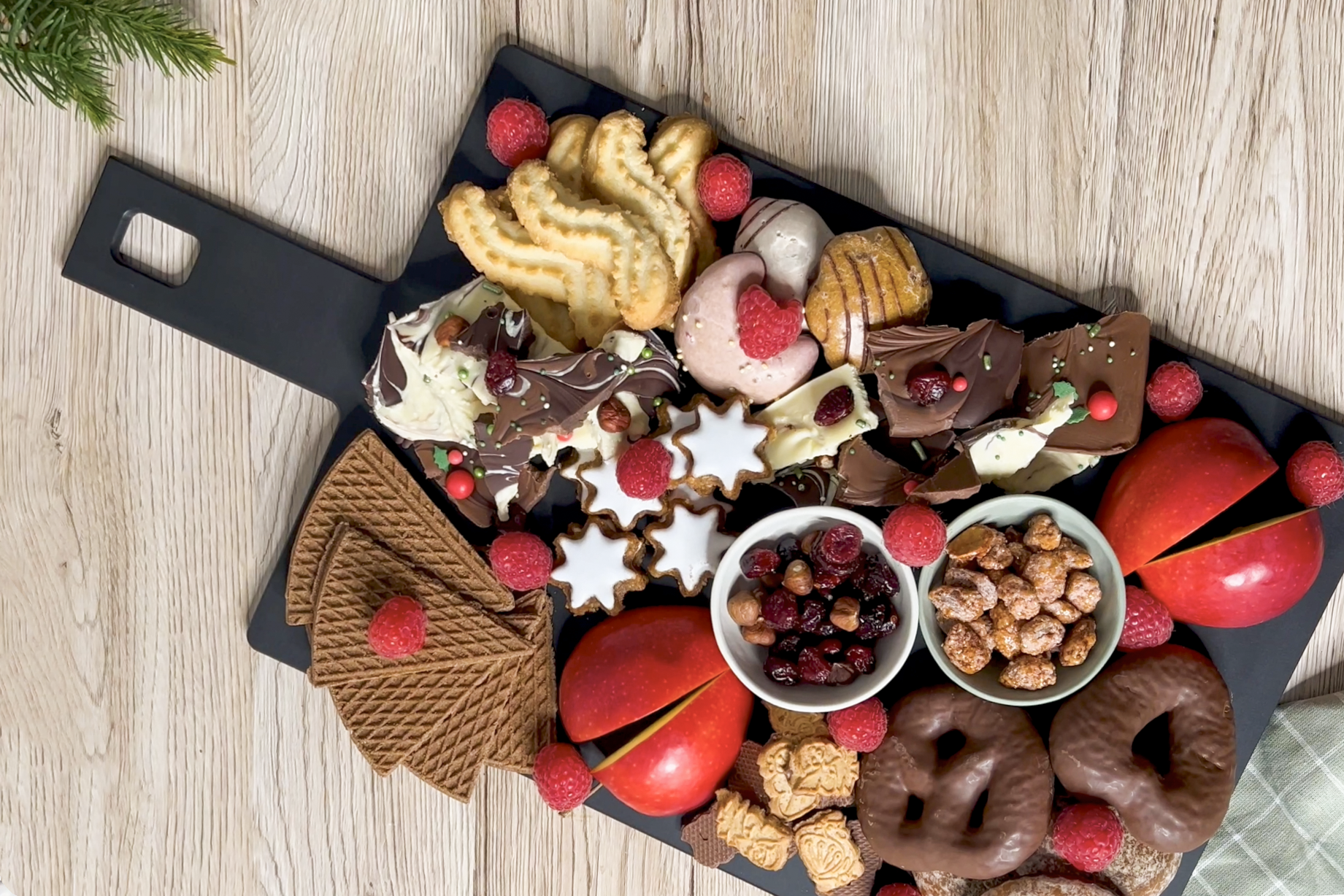Auf einem Schneidebrett mit Griff aus der Serie Cut & Serve liegen weihnachtliches Gebäck, Schokolade, halbierte Äpfel sowie zwei Schüsseln mit Beeren und Nüssen.