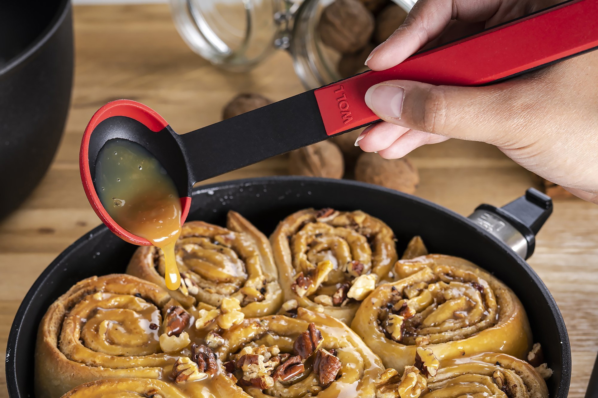 KU014_Zimtschnecken_2000x1334_RGBpx In einer runden Eco-Lite-QXR-Pfanne befinden sich Zimtschnecken, diese werden mit einem roten Cock it Saucenlöffel mit Karamellsoße übergossen.