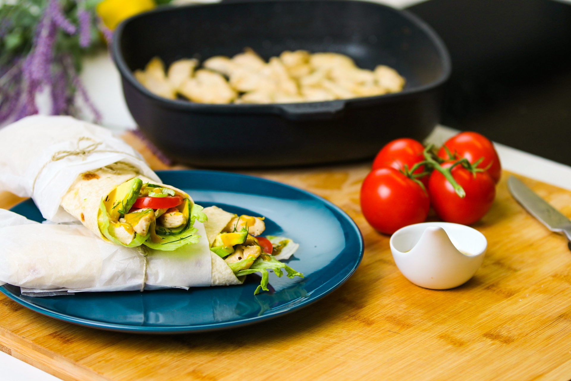Auf einem Teller befinden sich frisch zubereite Wraps, dahinter sieht man ganze Tomaten und eine viereckig Titan Best Pfanne.