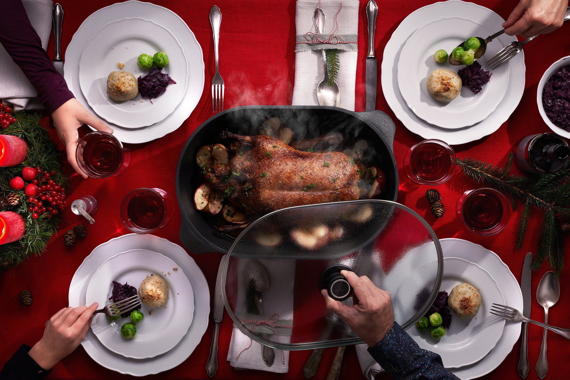 In einem Gussbräter der Serie Titan Best mit abgenommenem Deckel befindet sich ein Entenbraten in Orangensauce. Er steht in der Mitte eines weihnachtlich gedeckten Tisches. Drumherum liegen Besteck, Gläser und Teller, die bereits mit Klößen, Rotkohl und R