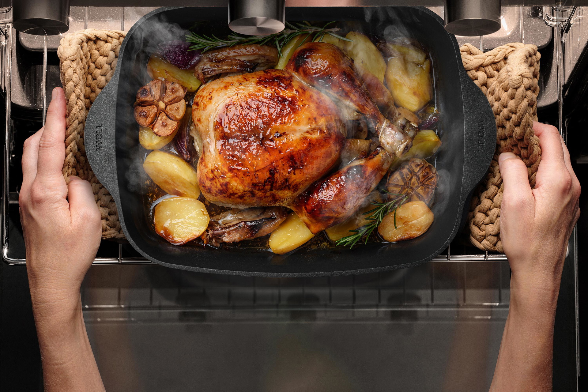 Auf einem Backofenrost steht ein Eco Logic QXR Bräter mit einem Geflügelgericht. Der Bräter wird mithilfe von Topflappen vom Backofenrost genommen.
