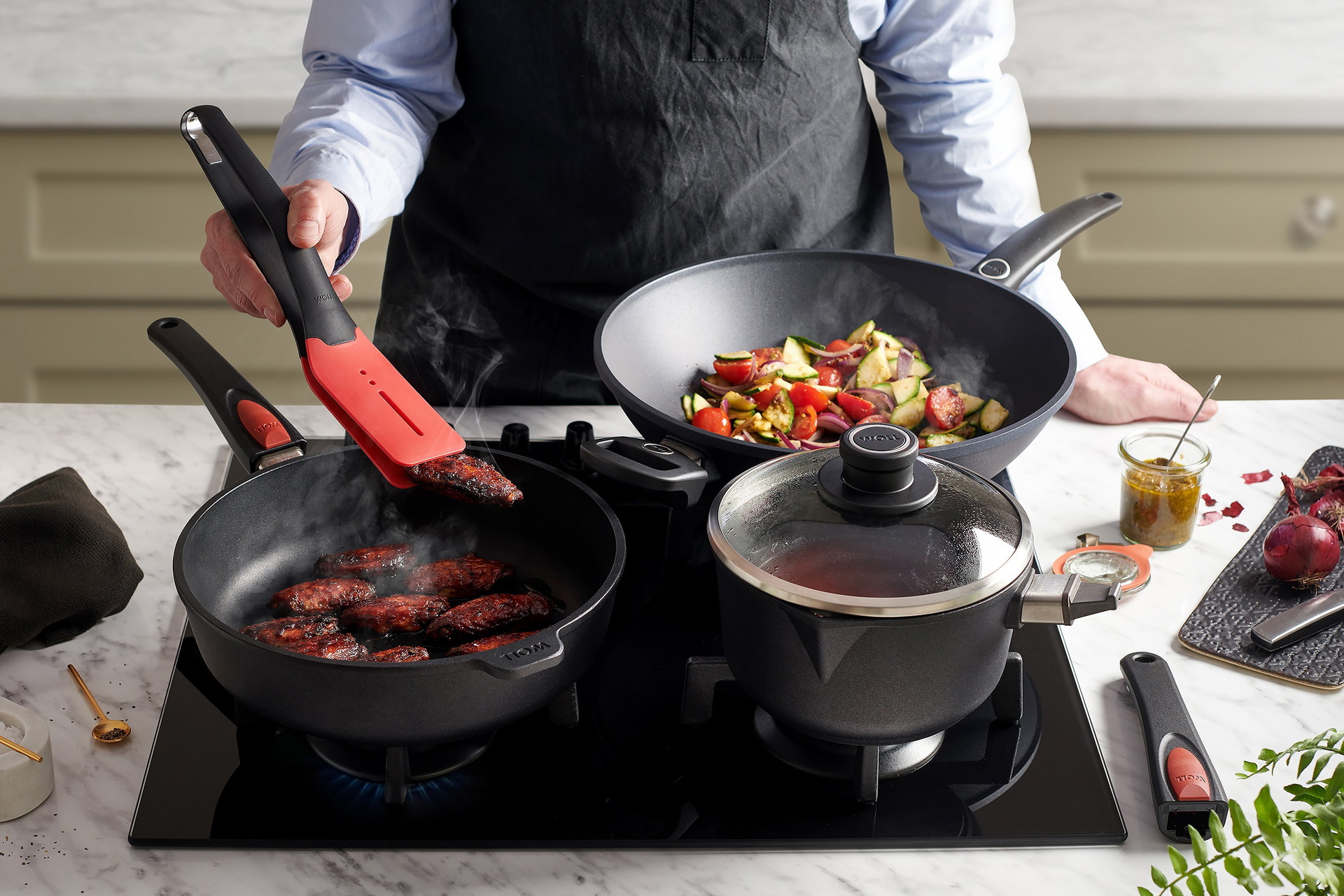 In einer heißen, runden Titan-Best-Pfanne mit abnehmbarem Stiel werden marinierte Chicken Wings zubereitet. In dem Stieltopf mit abgenommenem Stiel wird BBQ-Sauce zubereitet. Mit der Wok- und Rührpfanne mit festem Stiel wird außerdem warmer Pesto-Salat zu