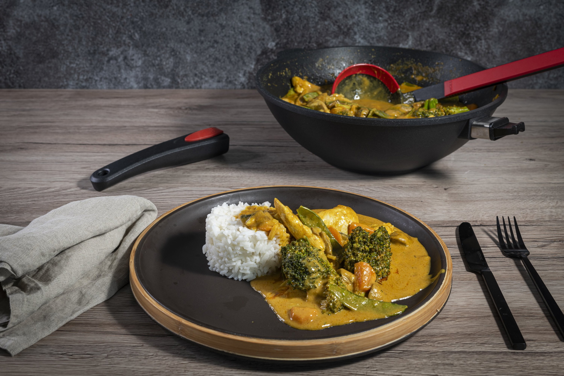 In einer runden Wok- und Rührpfanne der Serie Titan Best wurde frisches Erdnuss-Curry mit Hähnchen zubreitet. Daneben steht ein angerichteter Teller.