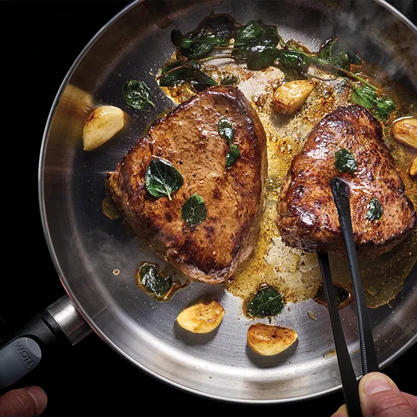 In einer heißen, runden Logic-Steel-Pfanne werden zwei Fleischstücke angebraten.