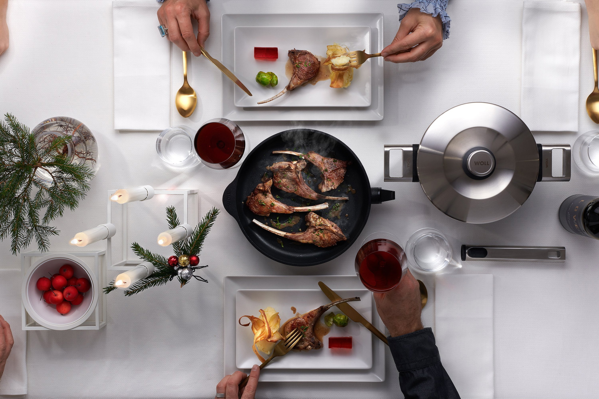 Auf einem Tisch steht eine runde, heiße Pfanne der Serie Logic mit abgenommenem Stiel. In dieser befinden sich frisch angebratene Lammkoteletts. Rechts daneben steht ein runder Logic-Topf mit Deckel. Der Tisch ist außerdem mit Tellern, auf denen das Geri