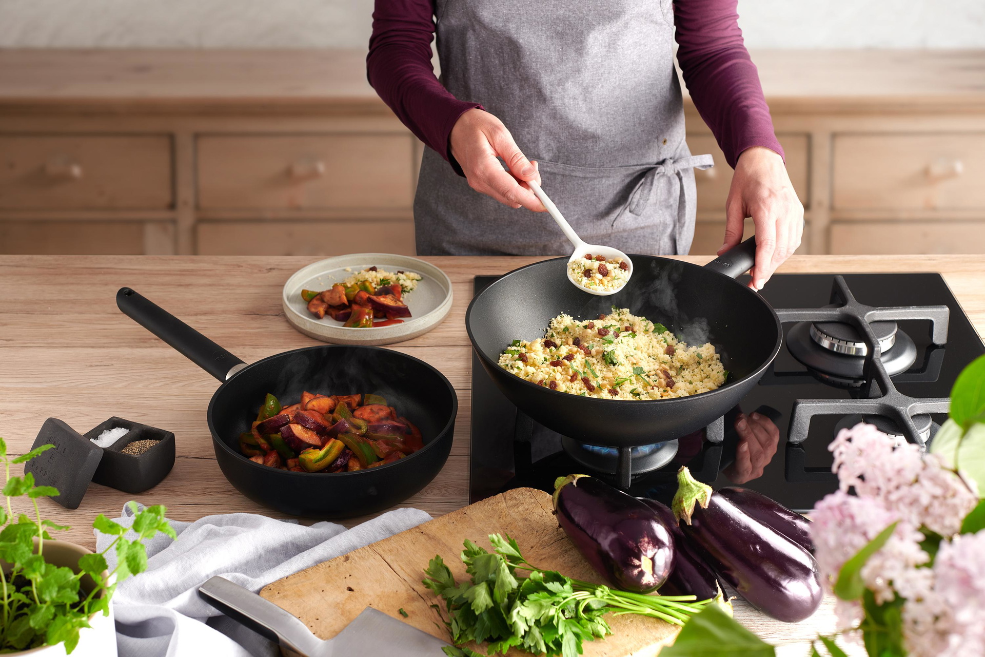 In einer runden Eco Lite QXR Wok- und Rührpfanne wird Couscous Salat zubereitet. Daneben steht eine weitere Eco Lite QXR Pfanne mit Gemüse.