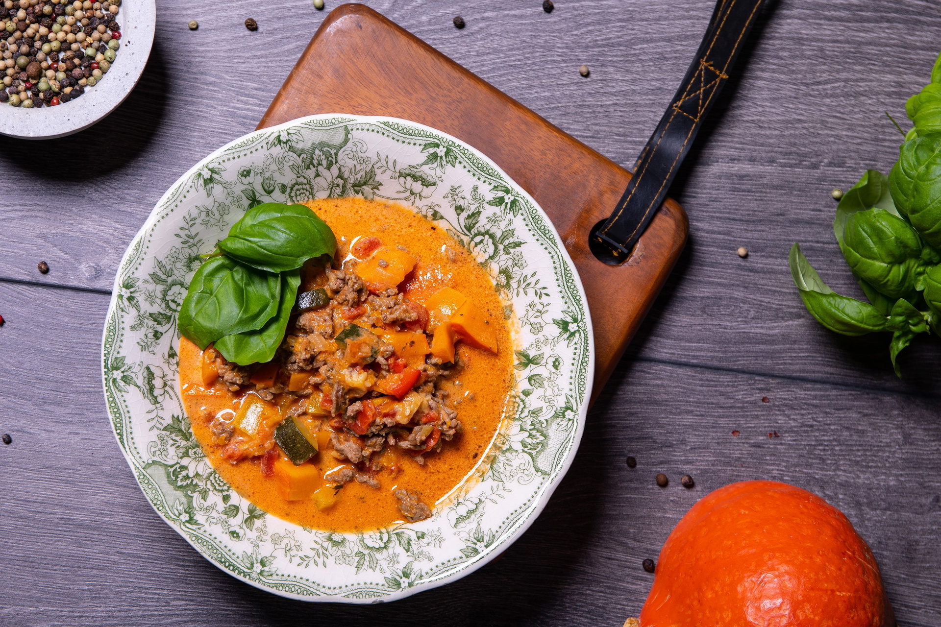 Auf einem Teller wurde eine frische Bauernpfanne mit Kürbis angerichtet. Drumherum liegen ein Kürbis, Pfefferkörner und Basilikum.