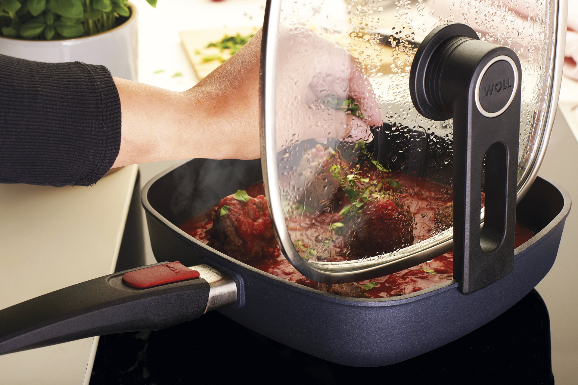 In einer viereckigen, heißen Diamond-Lite-Pfanne befindet sich frisch zubereitete Parmesan-Hackbällchen mit scharfer Tomatensauce. Der Glasdeckel ist mit der verlängerten Seite der Smart-Lid-Serie an der Kante der Pfanne eingehängt.