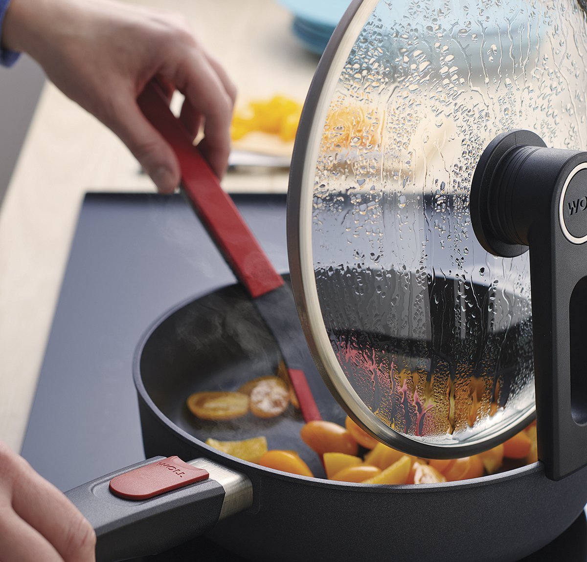 KU001_1200x1150_RGB In der runden Diamond Lite Pfanne wird ein Gericht mit einem roten Cock it Pfannenwender umgerührt. Der Smart Lid steht auf der Pfannenkante.