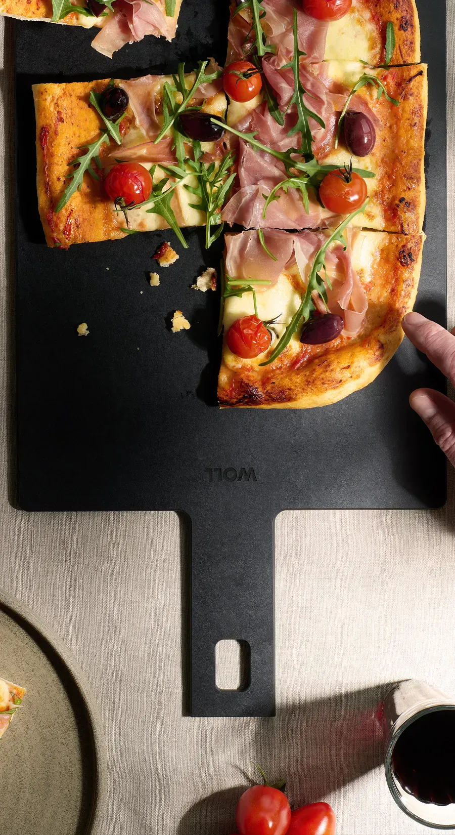 Auf dem Schneidebrett mit Griff der Serie „Cut & Serve” liegen frisch gebackene Pizzastücke. Außen herum stehen ein Glas, ein Teller und Tomaten als Dekoration.