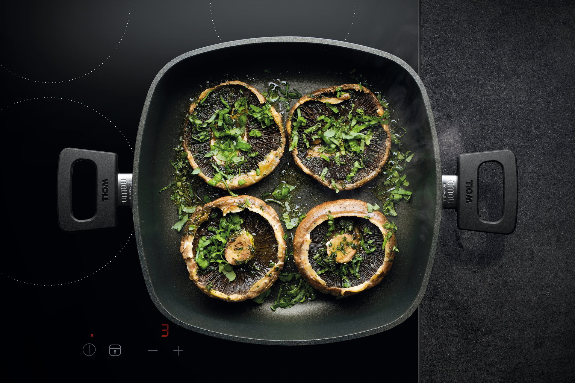 Auf dem Herd steht eine viereckige, heiße Pfanne der Serie Nowo mit abnehmbarem Stiel. Darin befindet sich frisch zubereitete Portobello-Pilze mit Kräuterbutter und frischem Basilikum.
