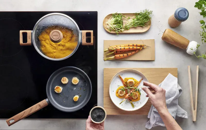 Die Jakobsmuscheln wurden in einer heißen, runden Pfanne der Serie Eco Logic QXR angebraten. Auf einem Teller, der neben dem Herd bereitsteht, werden sie auf einem Bett aus Karottenpüree serviert und mit einer halbierten, angebratenen Karotte garniert. Au