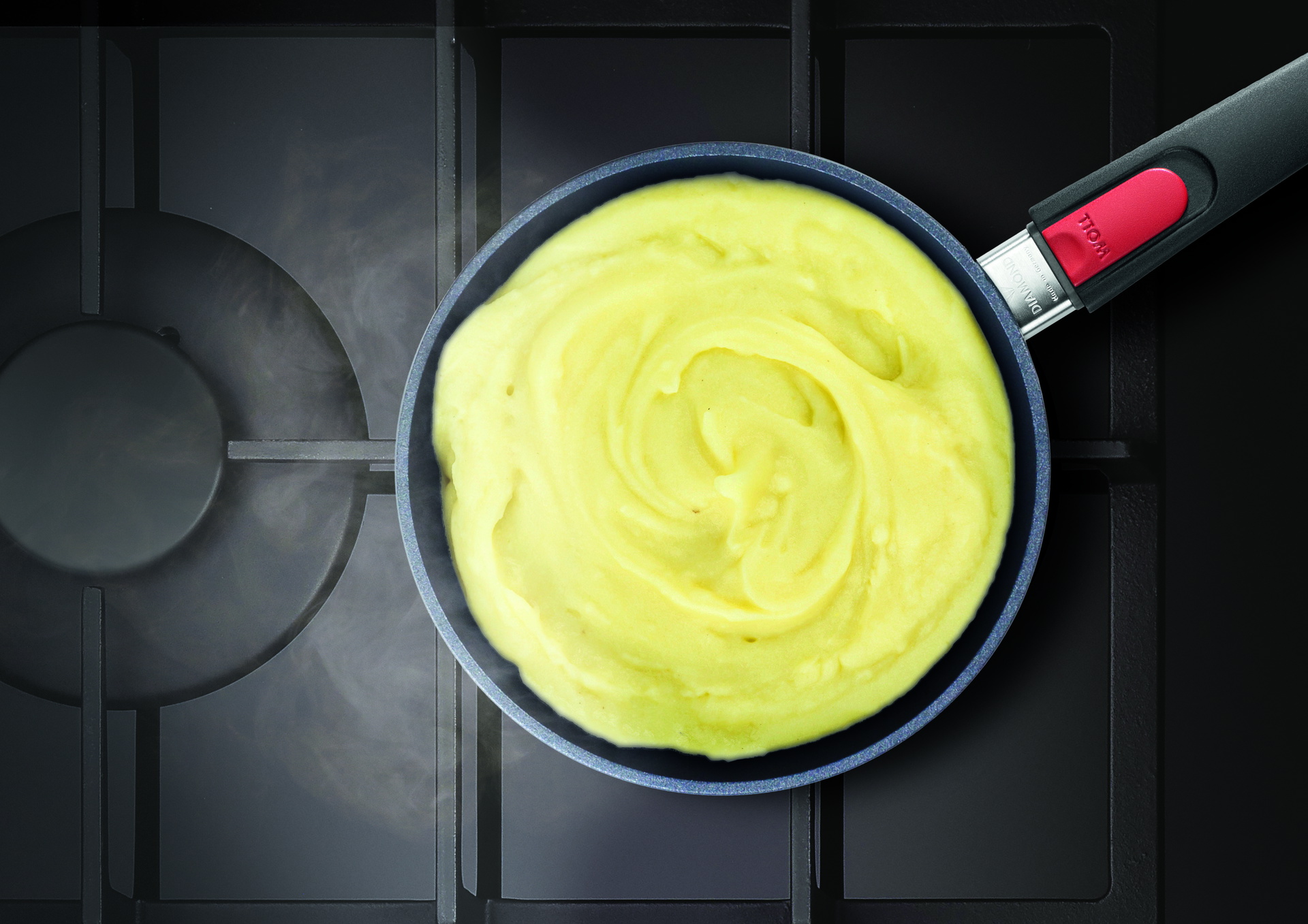 Auf dem Herd steht eine runde, heiße Diamond-Lite-Pfanne mit abnehmbarem Stiel ohne Deckel, in der sich frisches, dampfendes Kartoffelpüree befindet.