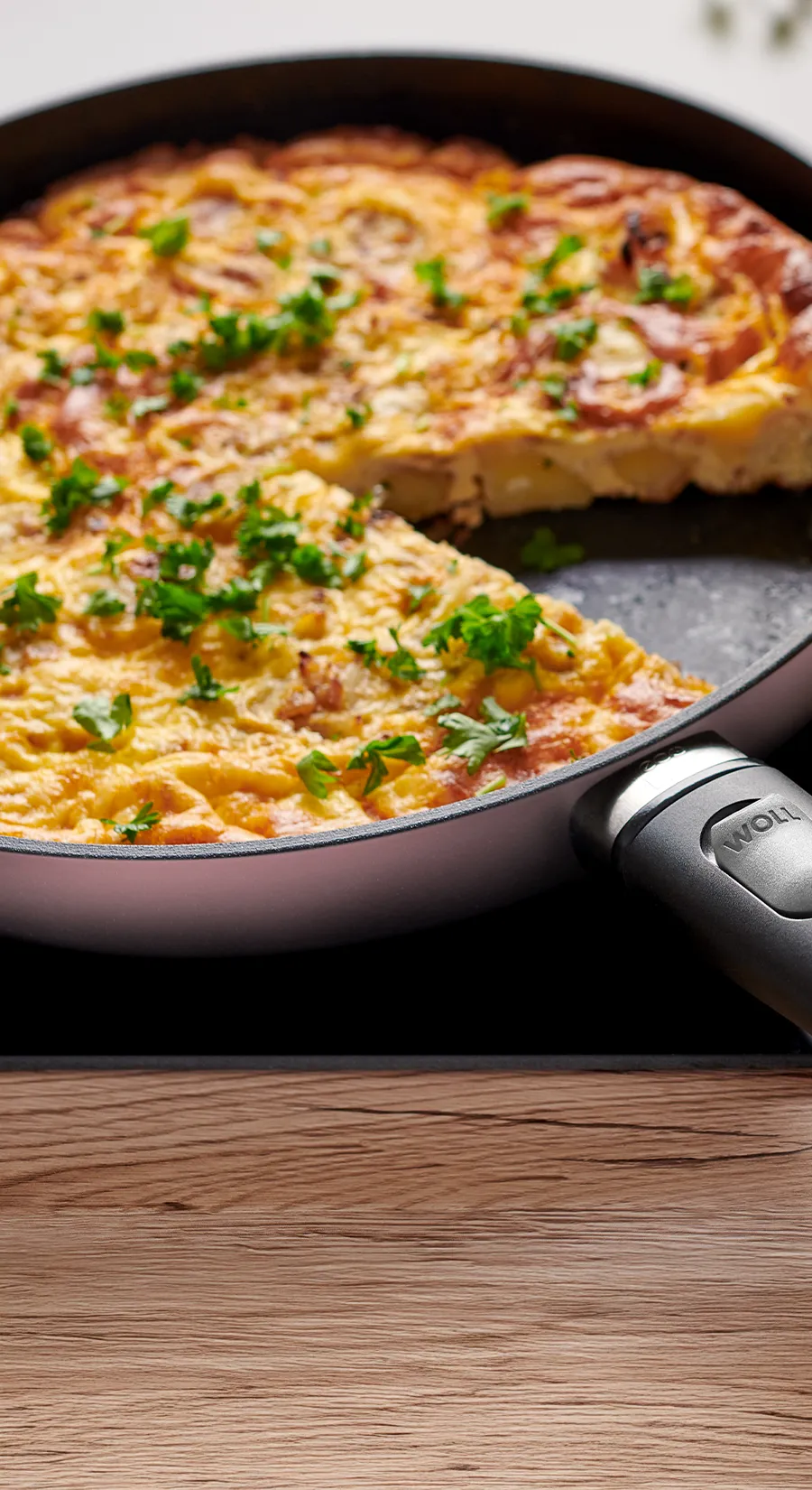 In einer runden Pfanne der Serie Ecolour mit abnehmbarem Stiel befindet sich eine frisch zubereitete spanische Tortilla. Ein Teil davon wird zusammen mit frischem Salat auf einem Teller serviert.