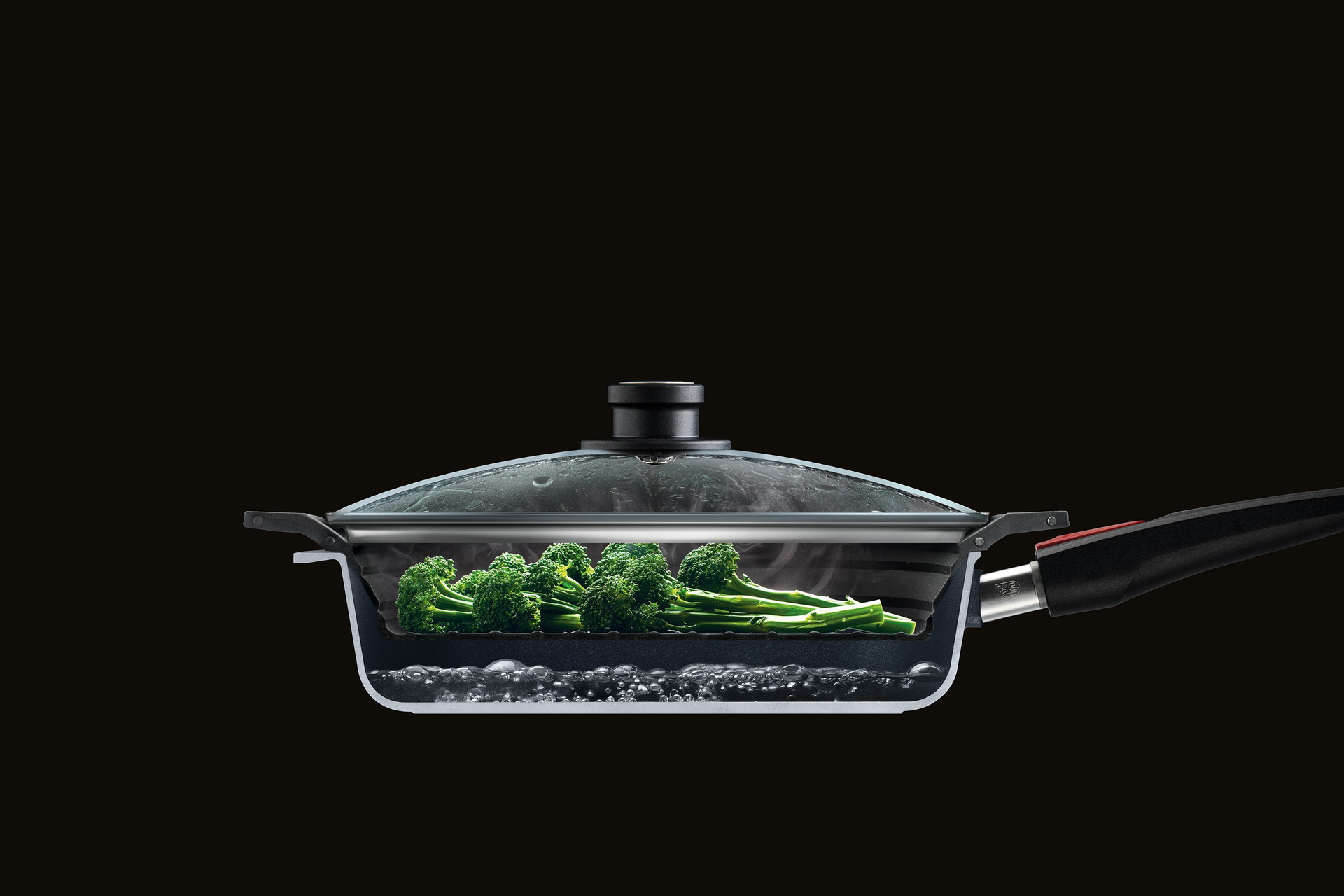 SI28F_Mood Im Querschnitt ist eine halbierte Wok Pfanne mit Glasdeckel zu sehen, in der Brokkoli mit dem Steam it multifunktionalen Silikoneinsatz gedämpft wird.