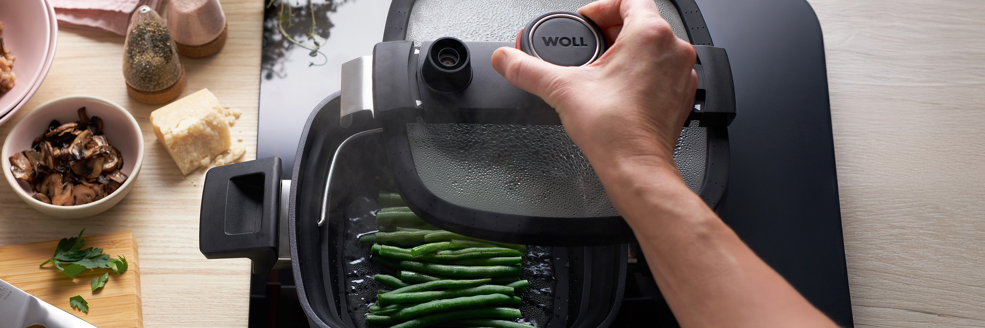 In einer viereckigen Kasserolle der Serie Diamond Active Lite werden in einem passenden Siebeinsatz Bohnen gedünstet. Auf der Arbeitsplatte stehen Salz- und Pfefferstreuer, Parmesan, eine Schüssel mit gebratenen Pilzen sowie ein Schneidebrett mit Messer.