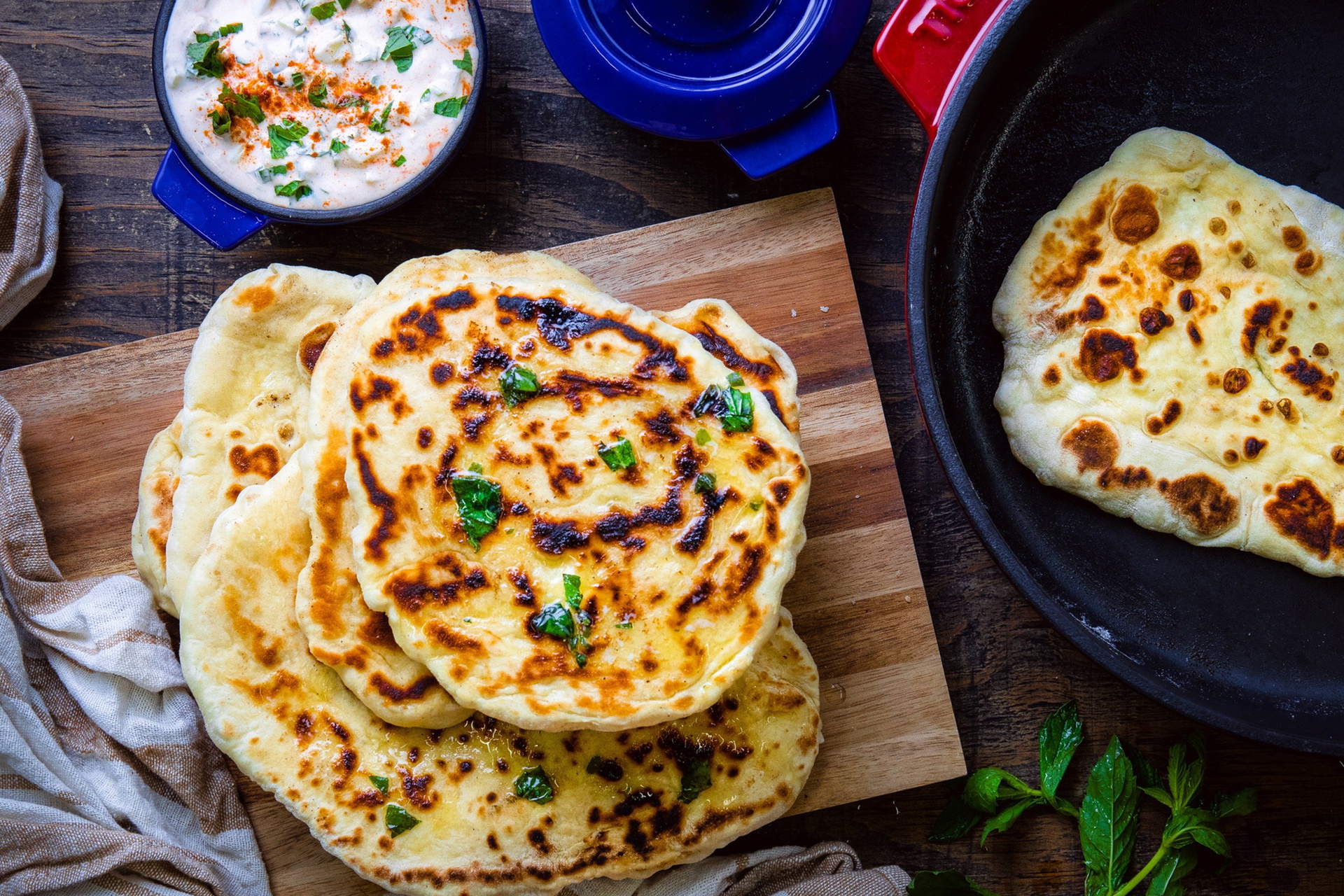 In einer runden Kasserolle aus der Serie Iron wurde frisches Naan-Brot zubereitet und auf dem Holzbrett daneben platziert. Darüber steht eine Mini-Kasserolle, die mit griechischem Joghurt gefüllt ist.