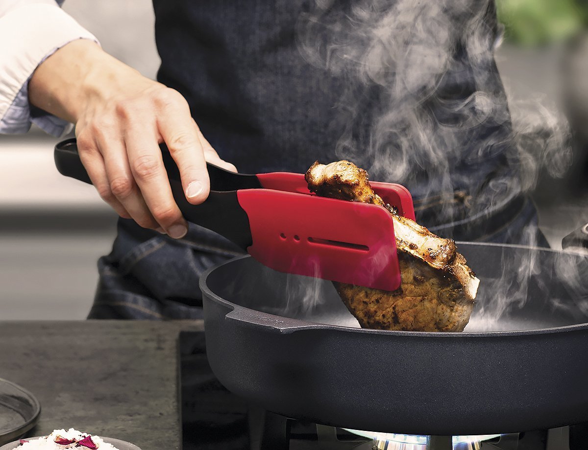 KU009_Mood_1200x920_RGB Ein dampfendes, angebratenes Stück Fleisch wird mithilfe der roten Cock it Küchenzange in der heißen Pfanne gewendet.