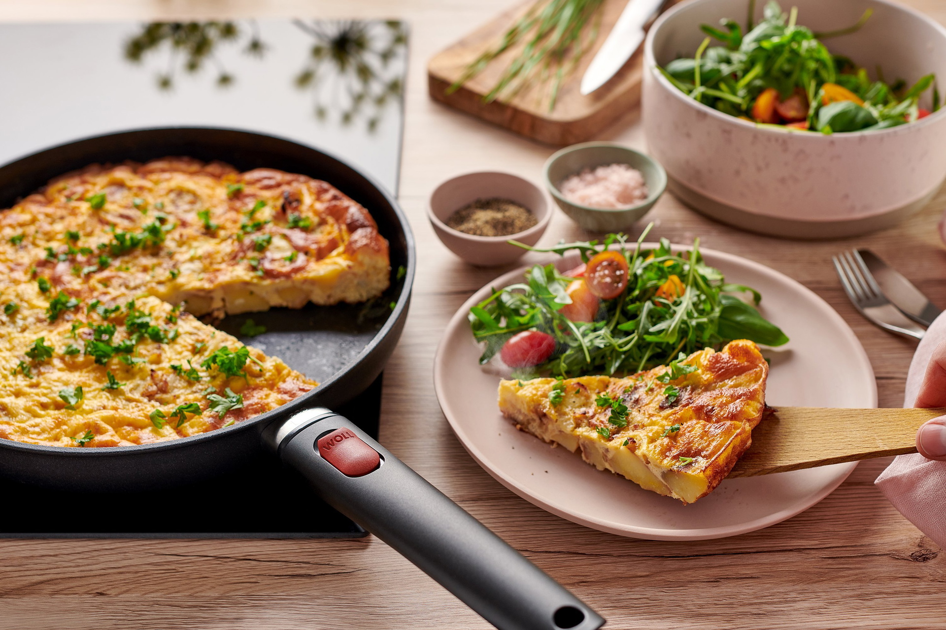 In einer runden Pfanne der Serie Eco Light QXR mit abnehmbarem Stiel befindet sich eine frisch zubereitete Spanische Tortilla. Ein Teil davon wird zusammen mit frischem Salat auf einem Teller serviert.