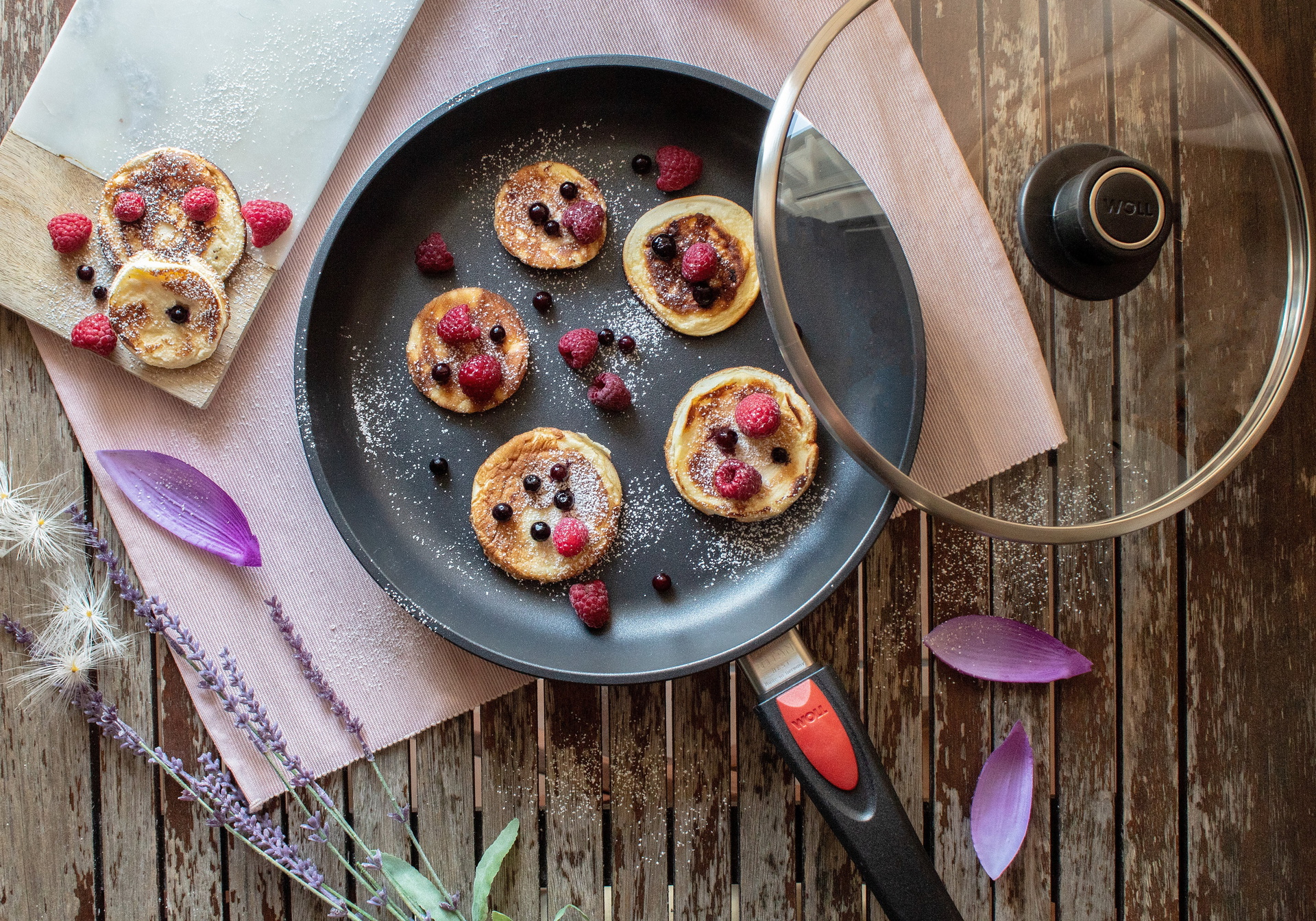 In einer runden Titan Best Pfanne mit abnehmbarem Stiel . Der Glasdeckel ist an den Pfannenrand angelehnt. In der Pfanne befinden sich frisch zubereitete Pancakes mit Beeren.