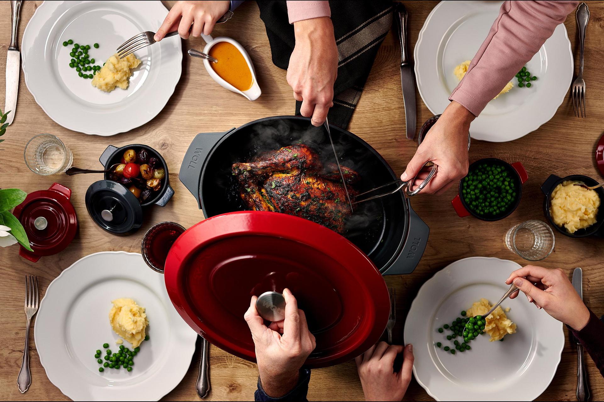 3426CI_110CI_Mood Auf dem Tisch steht ein roter Iron Bräter, in dem sich ein zubereitetes Geflügel befindet, das angeschnitten wird.