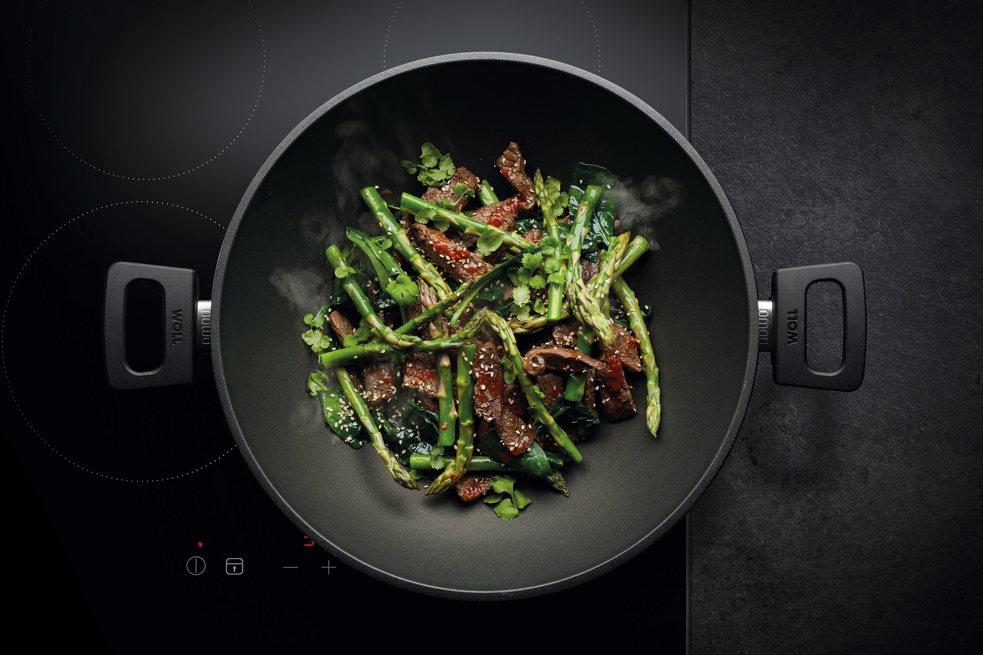 Auf dem Herd steht ein runder, heißer Wok der Serie Nowo. Darin befindet sich frisch angebratenes Rindfleisch mit Spargel.