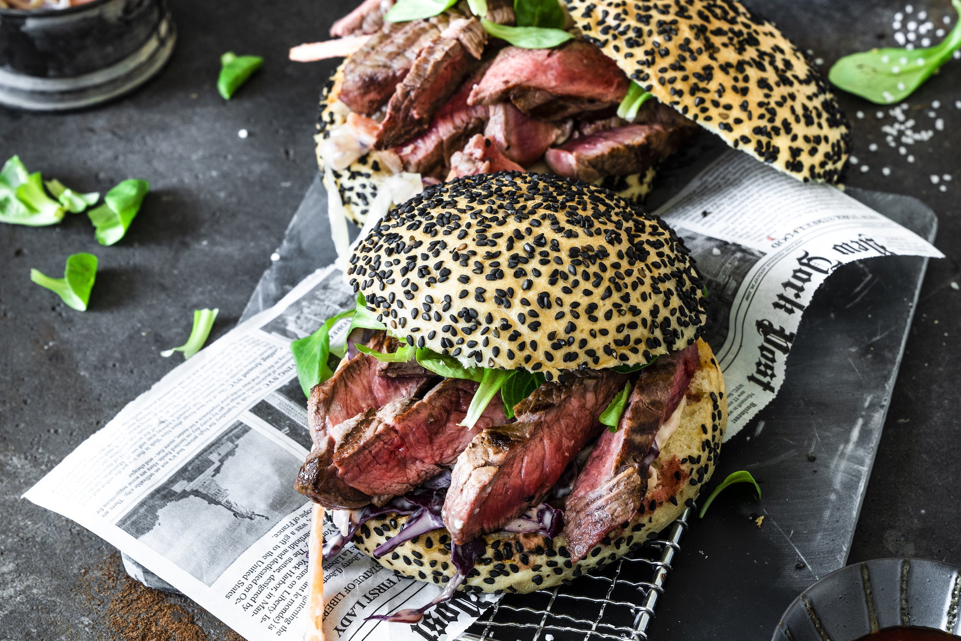Auf einem Rostund Zeitungspapier liegen zwei Mini Steak Burger mit Coleslaw.