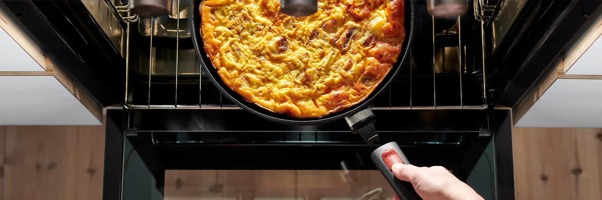 Eine runde, heiße Pfanne der Serie Eco Lite QXR steht mit einem dampfenden Gericht auf dem Rost des Backofens. Um die Pfanne aus dem Backofen zu nehmen, wird der abnehmbare Stiel wieder eingerastet.