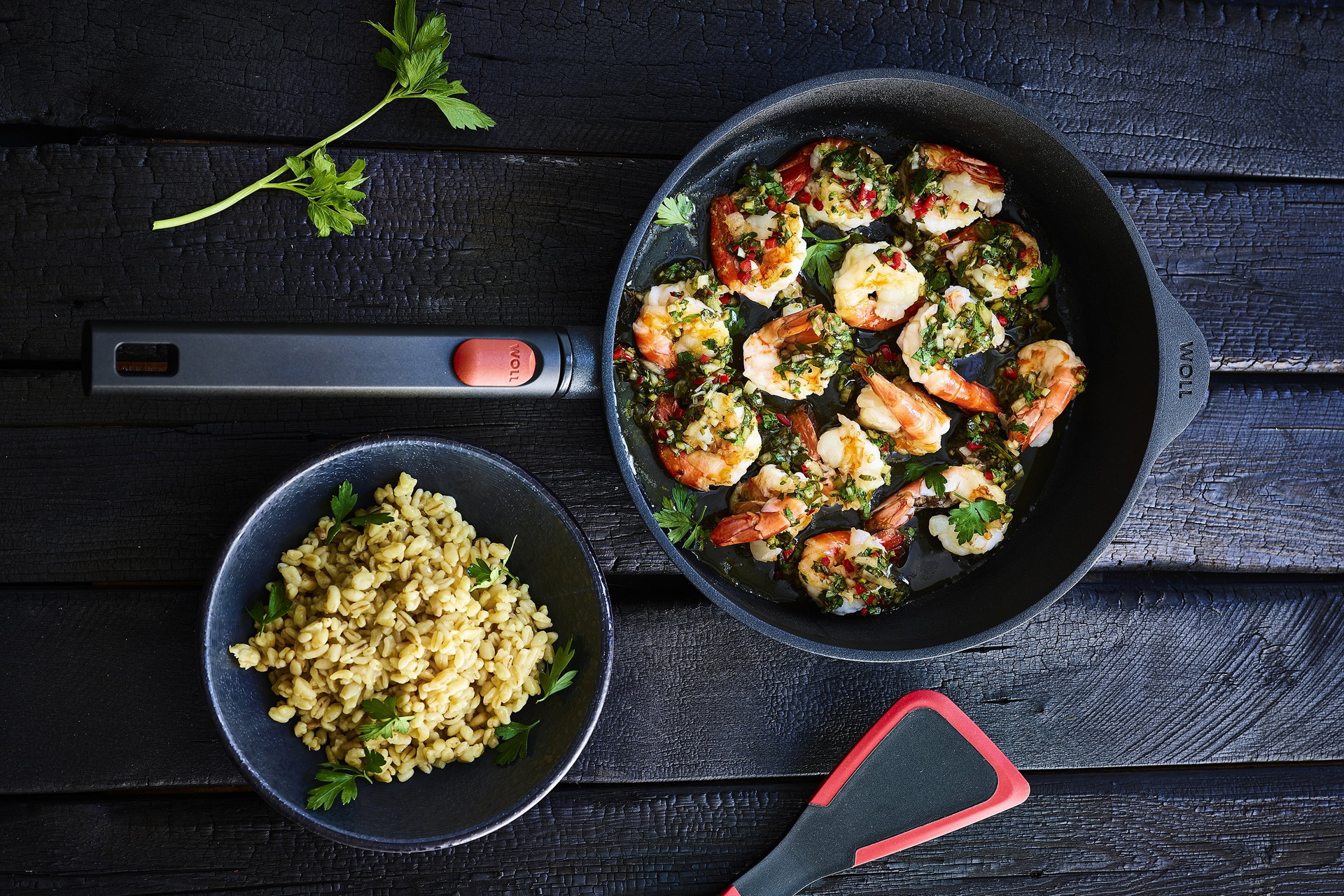 In einer runden, heißen Logic-Pfanne mit abnehmbarem Stiel wurden Garnelen mit Sonnenweizen zubereitet. Daneben steht eine Schüssel mit frischen Nudeln sowie ein Pfannenwender der Serie Cock it.