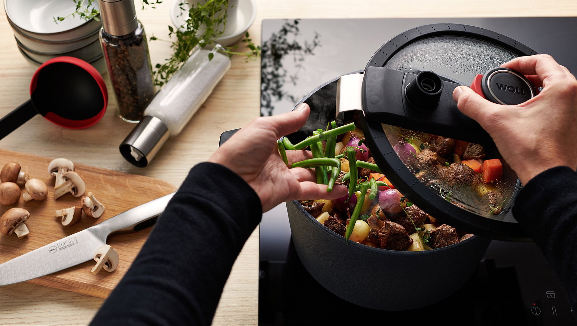 Auf dem Herd steht ein runder, heißer Niederdrucktopf der Serie Diamond Active Lite, in dem sich saftiges Rindergulasch befiindet. Der Deckel wurde abgenommen, um weitere Zutaten hinzuzufügen. Daneben liegen auf einem Holzbrett halbierte Pilze und ein Mes