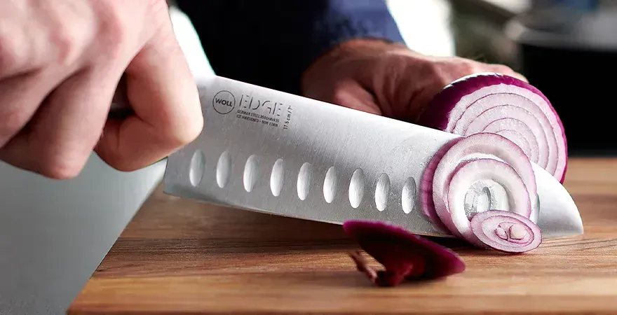 Auf einem Schneidebrett werden Zwiebeln mithilfe des Santokumessers der Serie Edge in dünne Scheiben geschnitten.