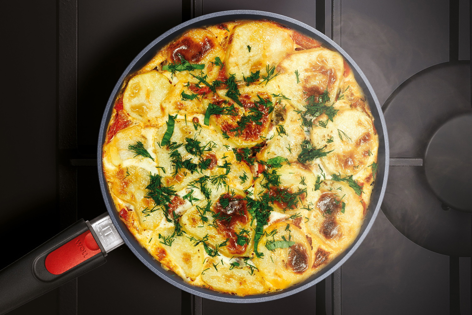 Auf dem Herd steht eine runde, heiße Diamond-Lite-Pfanne mit abnehmbarem Stiel ohne Deckel, in der frisches, dampfendes Kartoffel-Gratin zubereitet wurde.