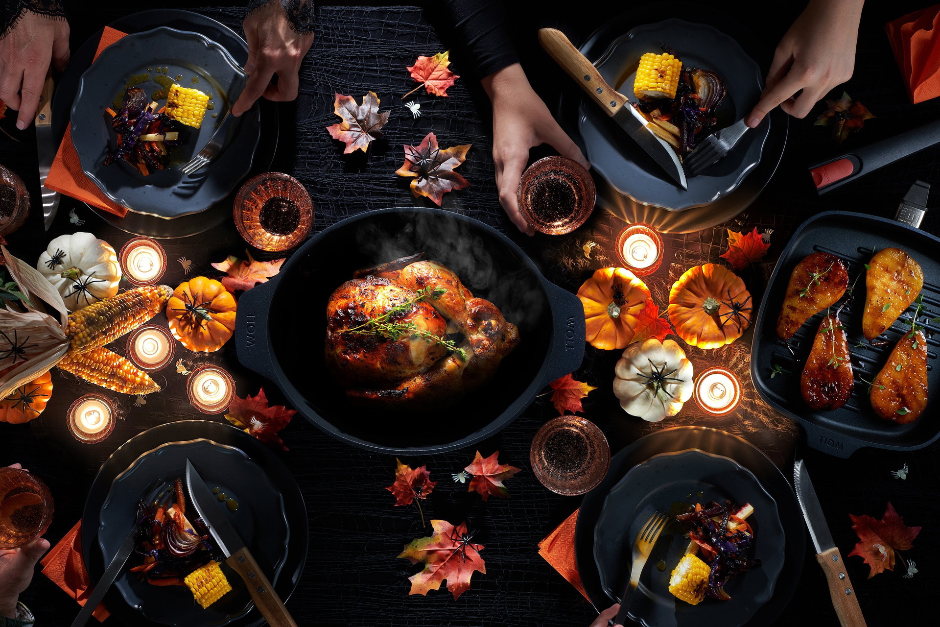 In einem Bräter der Serie Diamond Lite befindet sich frisch gebackenes Geflügel. Daneben steht eine Grillpfanne der gleichen Serie mit einem frisch angebratenen Stück Fleisch. Drumherum stehen gefüllte Teller und der Tisch ist mit Halloween-Deko geschmück