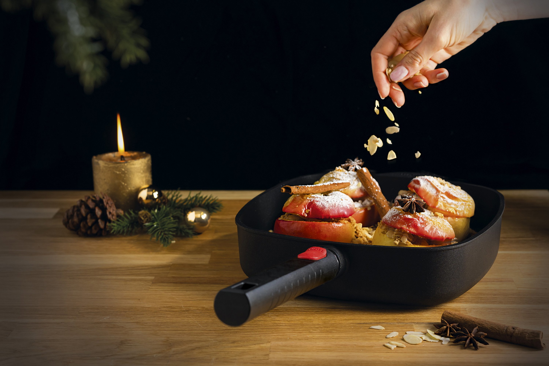 In einer viereckigen Pfanne der Serie Eco Logic QXR mit abnehmbaren Stiel liegen vier Bratäpfel, die mit Zimtstangen und Sternanis dekoriert sind. Darüber werden Mandelsplitter gestreut. Daneben steht eine brennende Kerze.