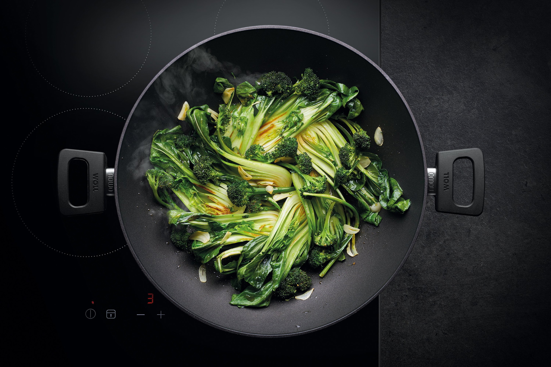 Auf dem Herd steht ein runder, heißer Wok der Serie Nowo. Darin befindet sich frisch angebratenes Gemüse.