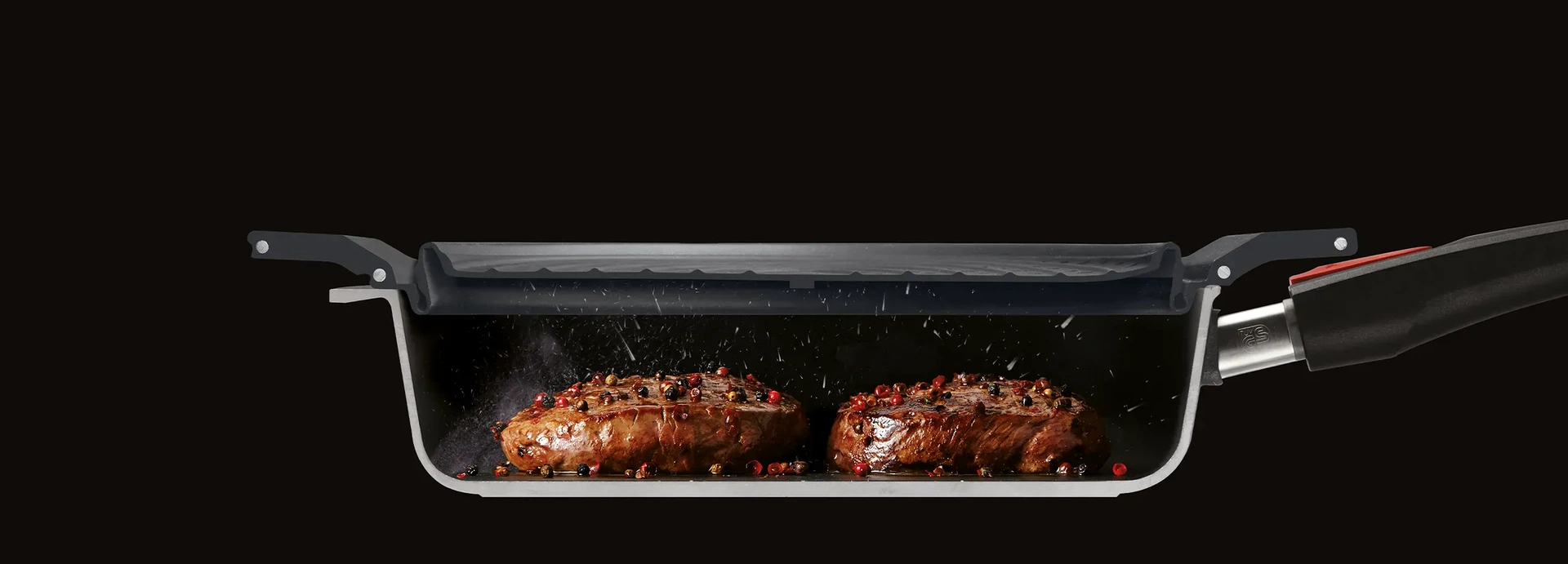 Im Querschnitt ist eine halbierte Pfanne zu sehen, in der zwei Stücke Fleisch angebraten werden. Der multifunktionale Silikoneinsatz der Serie Steam it dient als Spritzschutz.