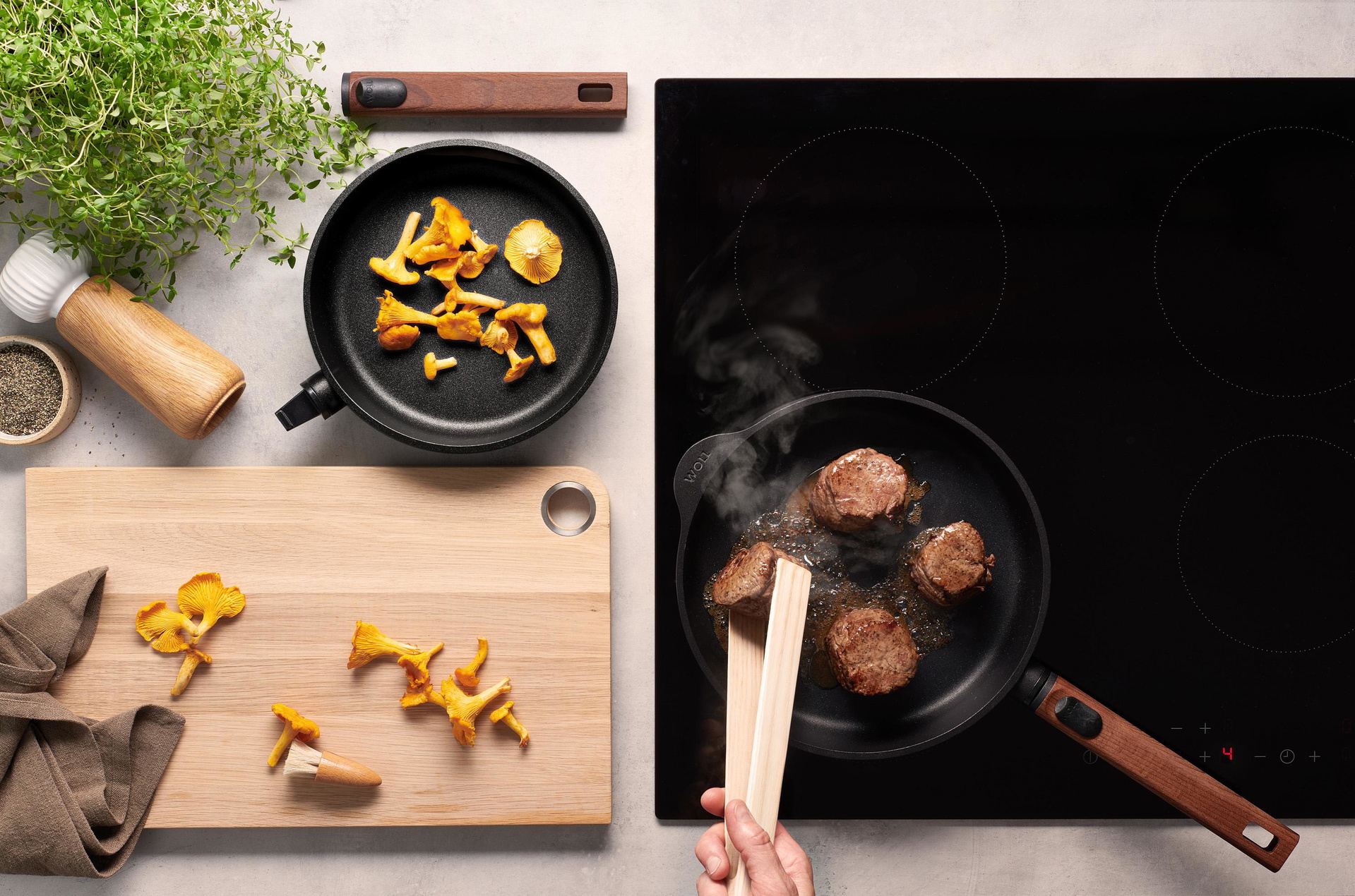 Eco Logic QXR Gusspfanne In einer runden Eco Logic QXR-Pfanne wird Fleisch angebraten und gewendet. In der Pfanne daneben liegen Pfifferlinge.