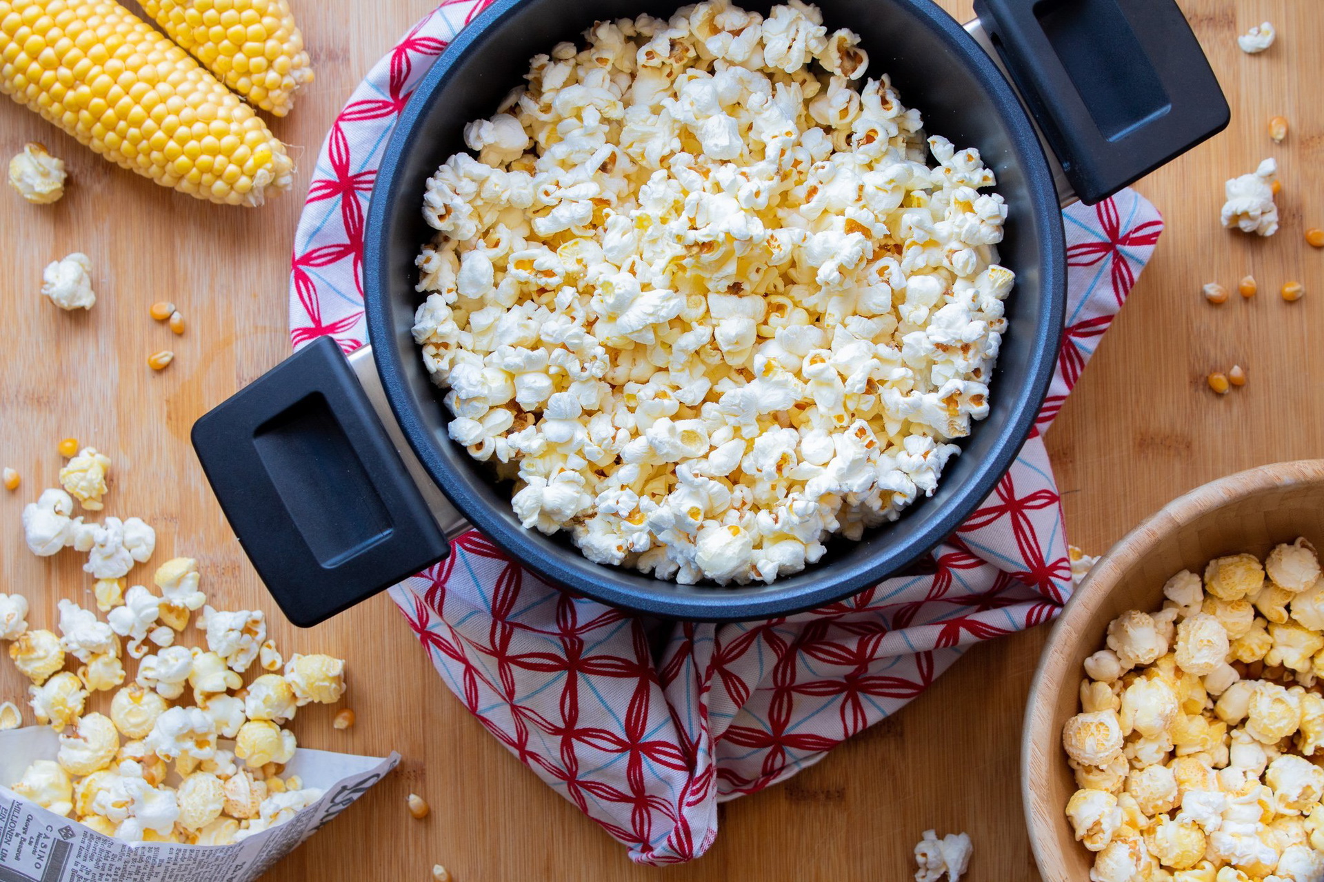 In einem runden Active-Lite-Topf wurde frisches Butterpopcorn zubereitet. Der Deckel wurde abgenommen. In einer Schüssel und einer Tüte befindet sich weiteres Popcorn.