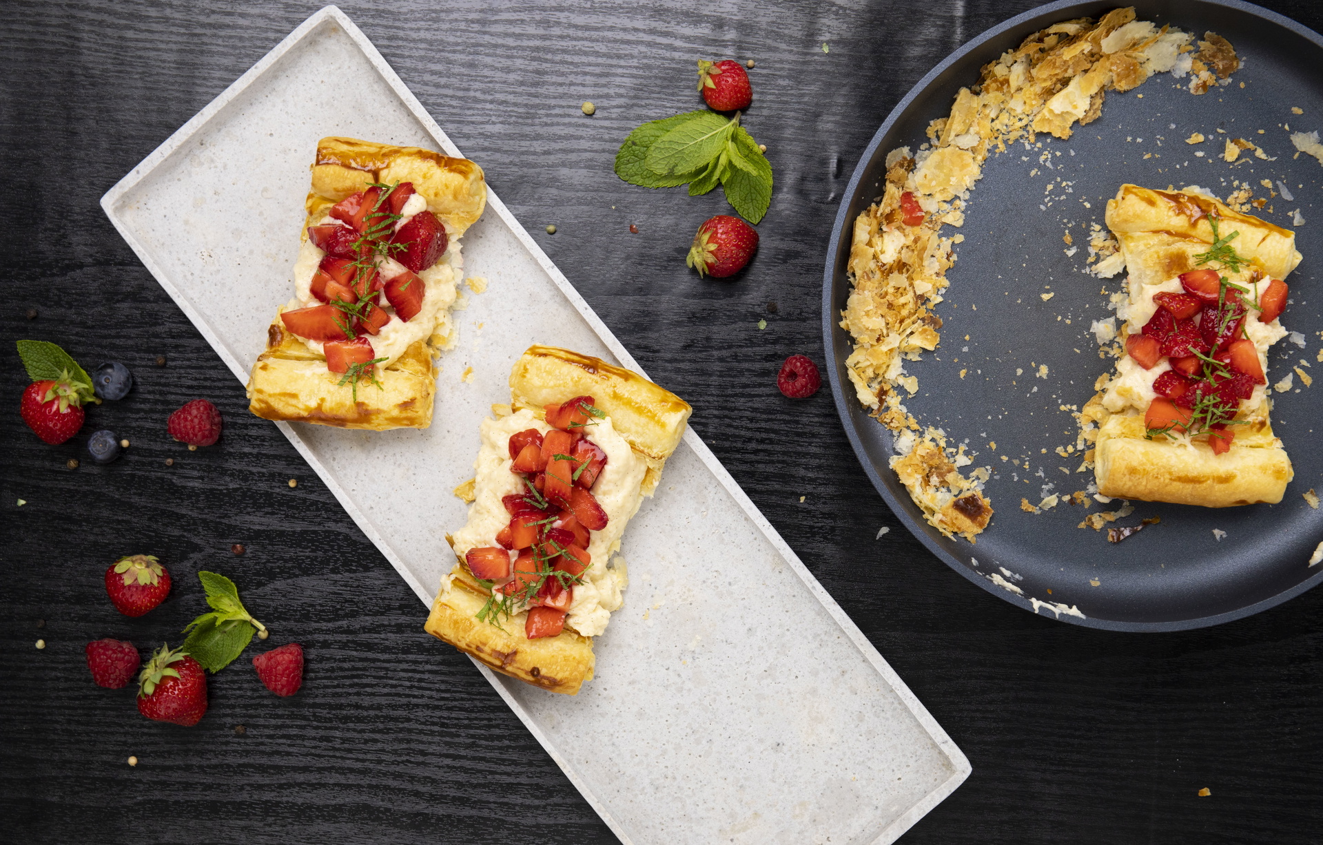 In einer runden Diamond-Lite-Pfanne mit abnehmbarem Stiel wurden frische Erdbeertörtchen mit Minze gebacken. Auf einem rechteckigen Teller wurden zwei dieser Törtchen angerichtet. Rundherum wurden frische Erdbeeren als Dekoration platziert.