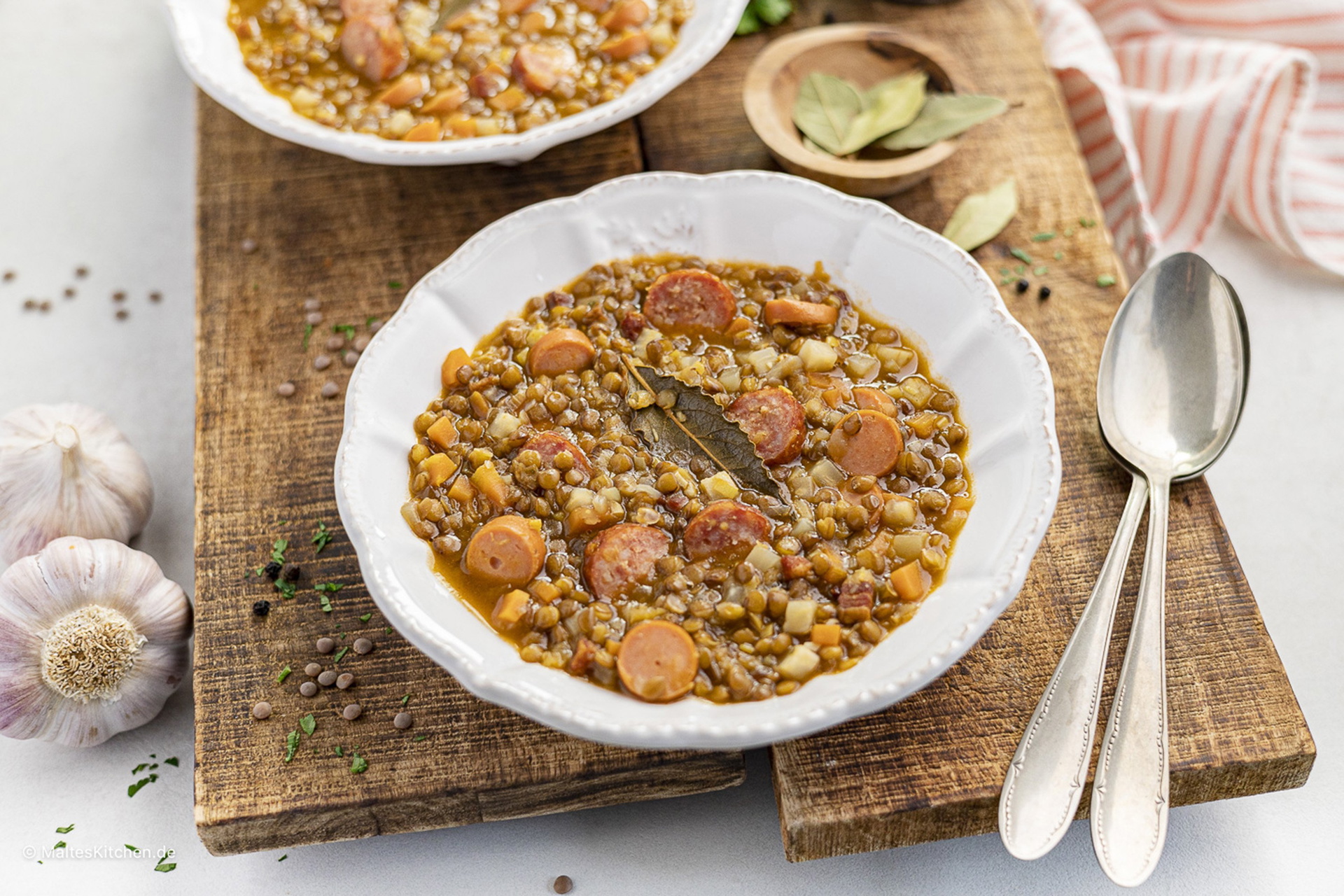 Auf einem Holzbrett stehen zwei Teller mit frisch gekochter Linsensuppe und Würstchen.
