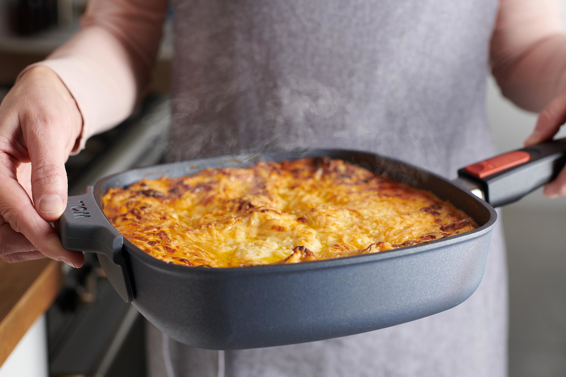 1624DPI_1624DPS_HG003_Mood In einer viereckige Diamond Lite Pfanne befindet sich ein überbackenes Gericht und wird mit zwei Händen gehalten. Der Silikongriff schützt vor Hitze.