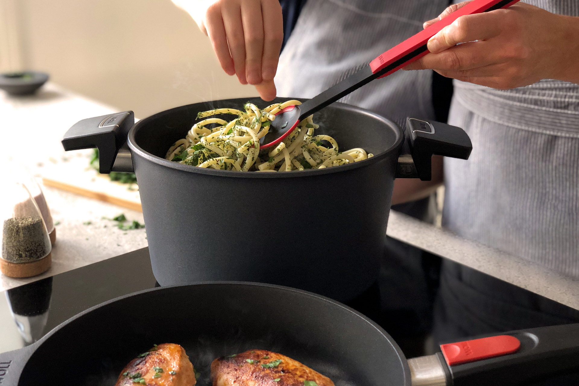 In einem Diamond Lite Topf werden Nudeln mit einem Cock it Kochlöffel umgerührt. Daneben steht eine runde Diamond Lite Pfanne.