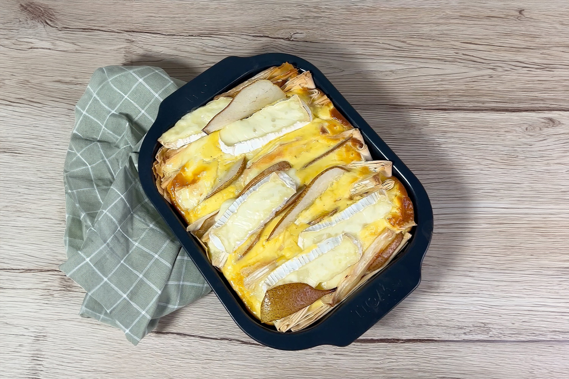 In einer Bratreine aus der Serie Roast it! befindet sich frisch gebackenes Crinkle Cake mit Birnen und Camembert. Ein Geschirrtuch liegt unter der Bratreine.