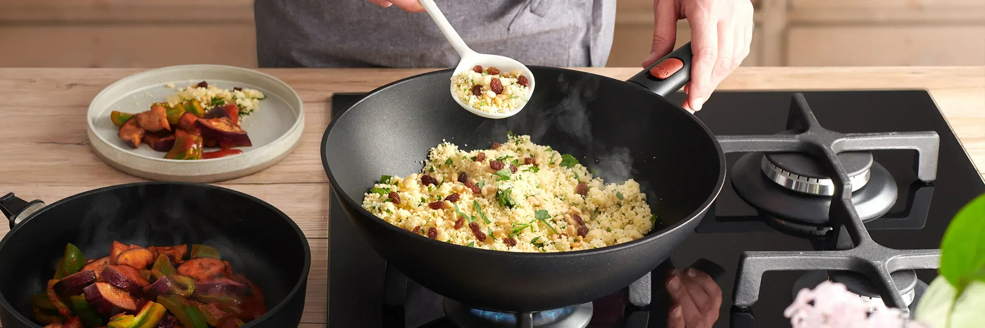 Auf dem Herd steht eine runde Wok-Pfanne aus der Serie Eco Lite QXR mit abnehmbarem Stiel. In ihr befindet sich ein dampfendes Gericht. Daneben stehen ein Teller, auf dem das Essen angerichtet wurde, und eine Pfanne mit abgenommenem Stiel, in der sich ebe