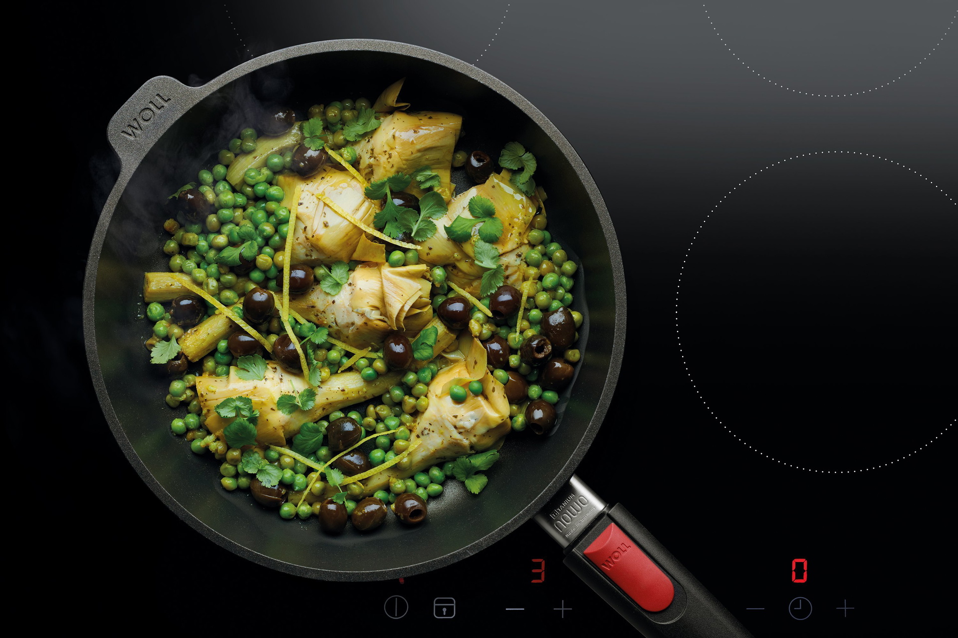 Auf dem Herd steht eine runde, heiße Pfanne der Serie „Nowo” mit abnehmbarem Stiel. Darin befindet sich ein frisch zubereiteter mediterraner warmer Salat.