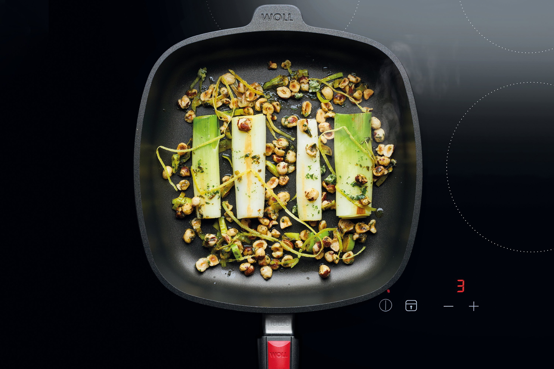 Auf dem Herd steht eine viereckige, heiße Pfanne der Serie Nowo mit abnehmbarem Stiel. Darin befindet sich frisch gebratener Lauch mit Haselnüssen, Kräuterbutter und Zitrone.
