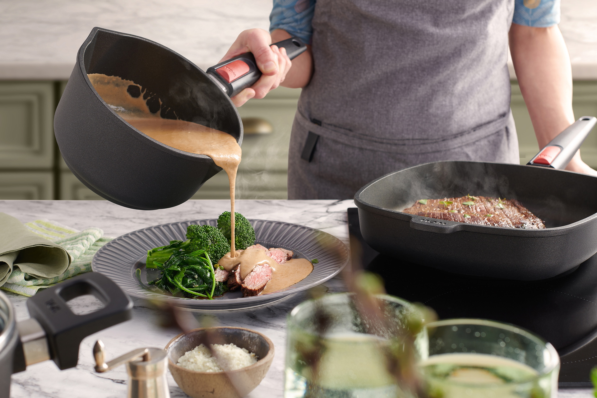 In der viereckigen Nowo Titanium Pfanne mit abnehmbarem Stiel wird das Fleisch scharf angebraten. Parallel dazu wird aus dem Nowo Titanium Stieltopf eine warme Sauce auf einen bereits portionierten Teller gegossen. Auf dem Teller liegen das dampfende Flei