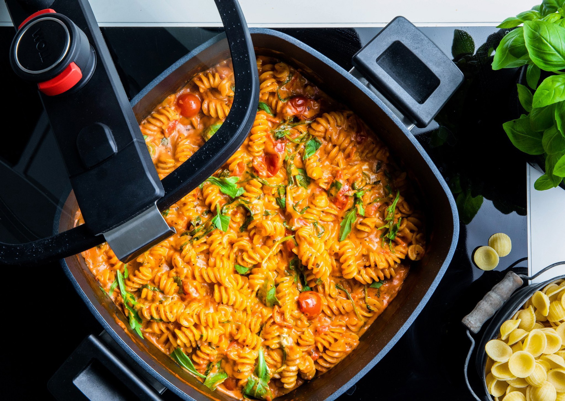 Auf dem Herd steht ein heißer,viereckiger Niederdrucktopf der Serie Diamond Active Lite. Der Glasdeckel wird von einer Hand angehoben. In dem Topf befindet frisch zubereitete One Pot Pasta.