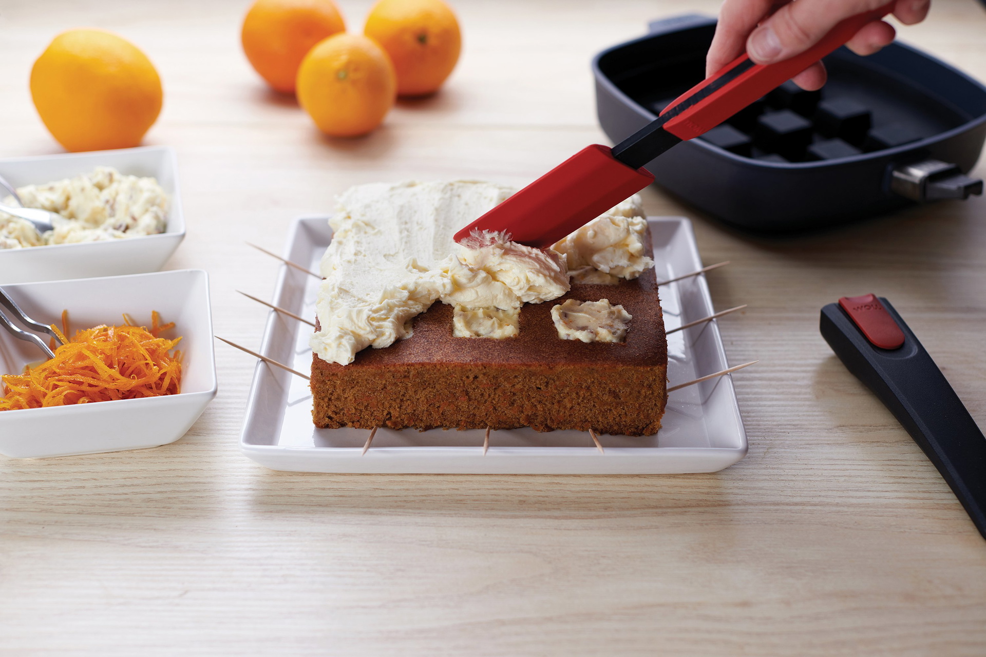 Bake-it_spreading_3000x2000_RGB Mit dem Cock it Teigschaber wird die Creme auf dem frisch gebackenen Kuchen verteilt. Daneben steht eine Diamond Lite Pfanne mit Silikon-Backeinsatz.